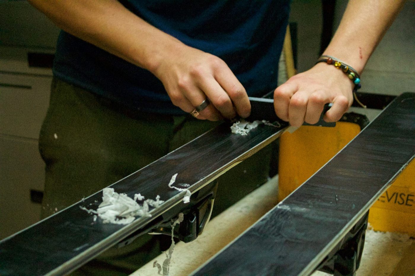 Technician scraping fresh wax from a pair of skis on a workbench (stock placeholder)